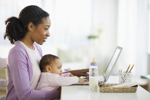 Mixed race woman holding baby and using laptop