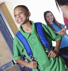 Pround young boy walking into school with students