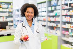 African American pharmacist holding apple and looking at camera.