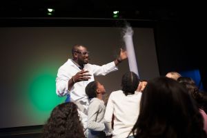 Children watching scientist demonstrating liquid nitrogen cloud in science center theater