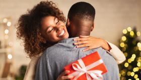Thankful afro woman with christmas gift hugging husband at home